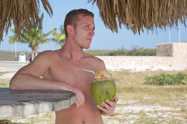 Young man on the beach drinking from coconut — Stock Photo, Image