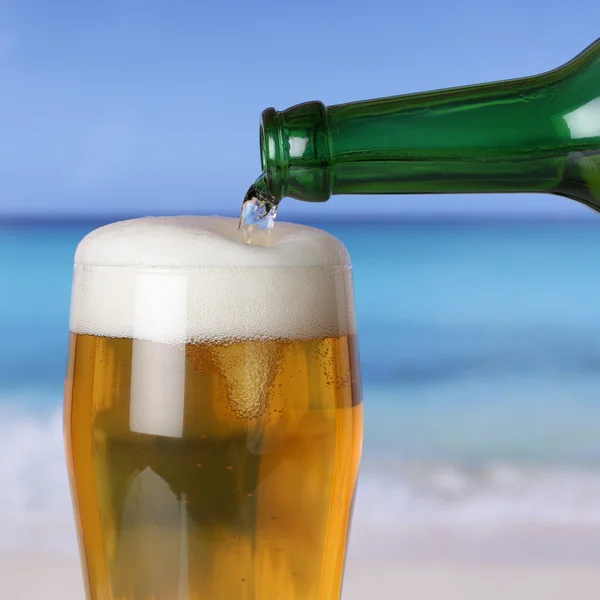 Öl hälla från flaska i glas på stranden och havet — Stockfoto