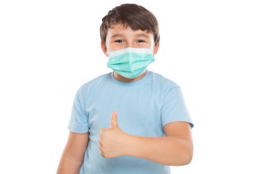 Coronavirus 'a karşı yüz maskesi takan küçük bir çocuk beyaz bir arka planda Corona Virüsü' nün baş parmağını gösteriyor.