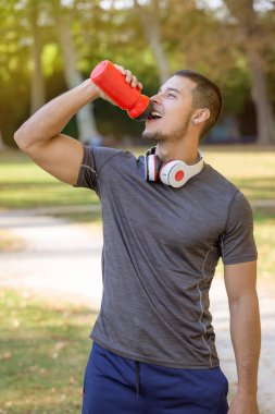 Koşucu gülümsüyor genç latin adam su içiyor portre çalışıyor spor antrenmanı formatında dışarıda spor yapıyor.