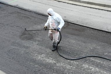 Beyaz korumalı, yol yüzeyine sıvı zift püskürten işçiler.