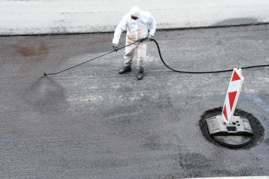 Beyaz korumalı, yol yüzeyine sıvı zift püskürten işçiler.