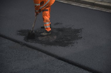 Yol işçisi asfalt bir yol döşeyip, fırça ve kürekle çalışıyor.