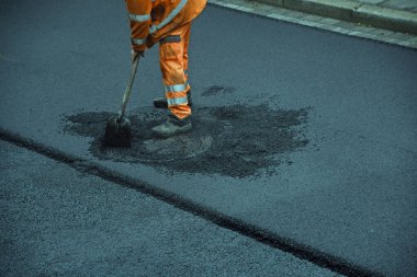Yol işçisi asfalt bir yol döşeyip, fırça ve kürekle çalışıyor.