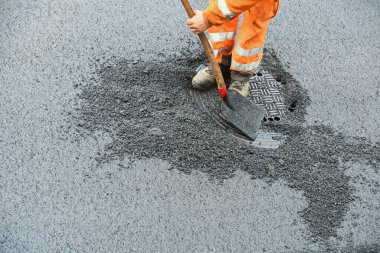 Aspalt Yolu inşaatında rögar kapağını açan kürekli bir işçi. 