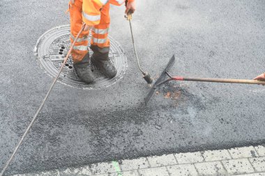 Propan yakıcılı işçi asfalt yüzeyi düzleştiriyor.