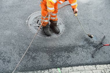 Propan yakıcılı işçi asfalt yüzeyi düzleştiriyor.