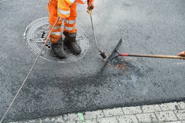 Propan yakıcılı işçi asfalt yüzeyi düzleştiriyor.