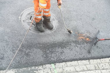 Propan yakıcısı olan işçiler asfalt yol yüzeyi döşüyorlar.