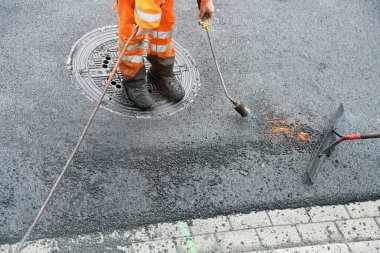 Propan yakıcısı olan işçiler asfalt yol yüzeyi döşüyorlar.