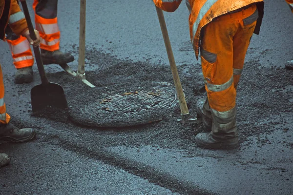 Adamlar kazma ve kürekle yol yüzeyindeki rögar kapağında çalışıyorlar.