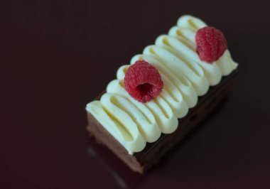Delicious cake with two raspberries on top on dark red table