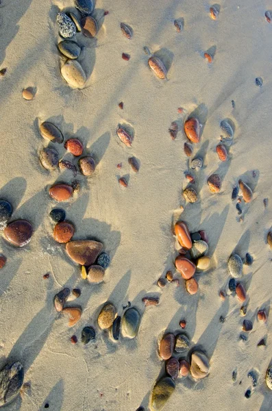 Kleurrijke natte keien rubed door golven in zee zand. — Stockfoto