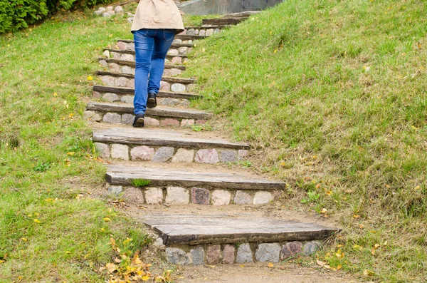 Mulher pernas azul jeans subir pedra madeira escadas — Fotografia de Stock