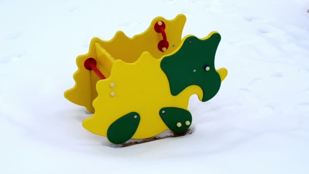 Colorful playground dinosaur shape swing toy move snow winter — Stock Video