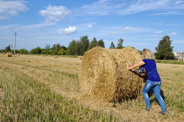 Vrouw jeans verplaatsen push baal stro landbouw veld — Stockfoto