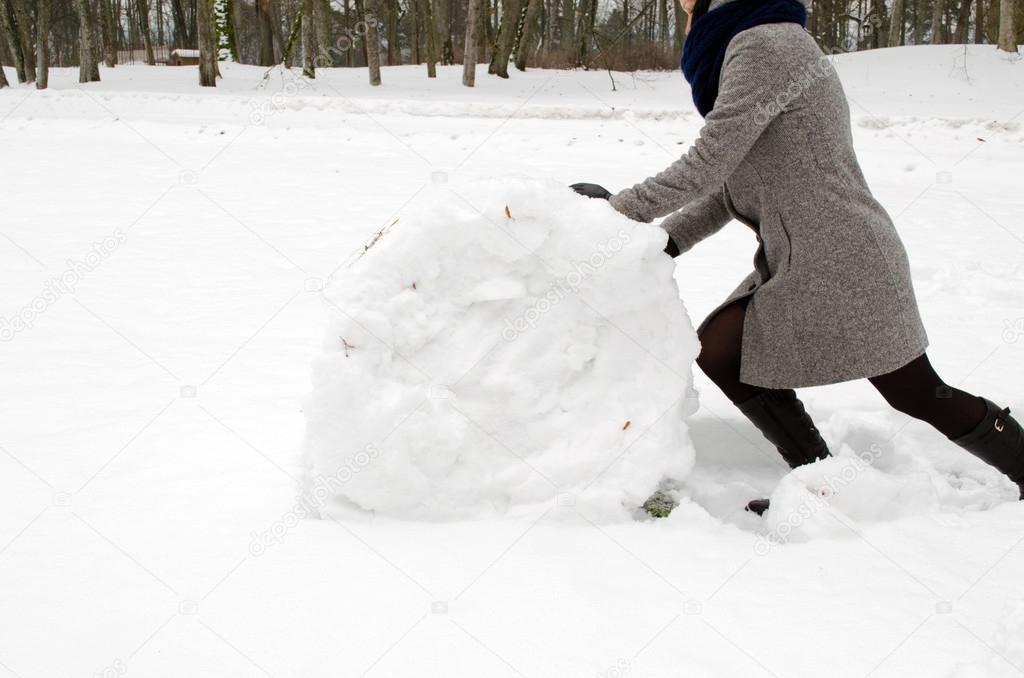 woman grey coat push big snow roll winter meadow