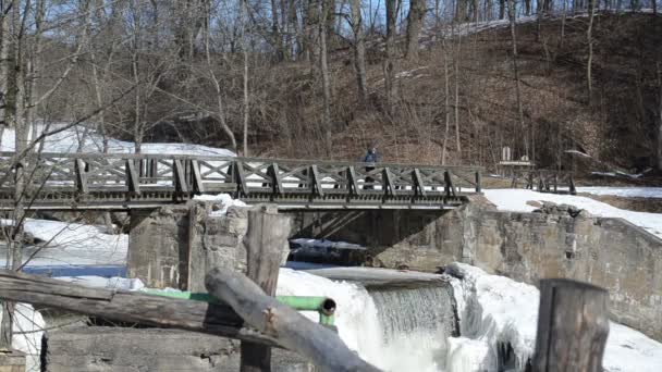 Kid backpack bag walk retro wooden bridge frozen river waterfall — Stock Video