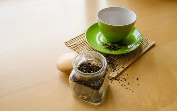 Herbes dans un bocal en verre et thé renversé près de tasse sur plateau en bois — Photo