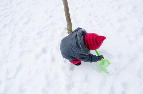 赤い帽子のシャベルを持つ少女雪を掘る — ストック写真