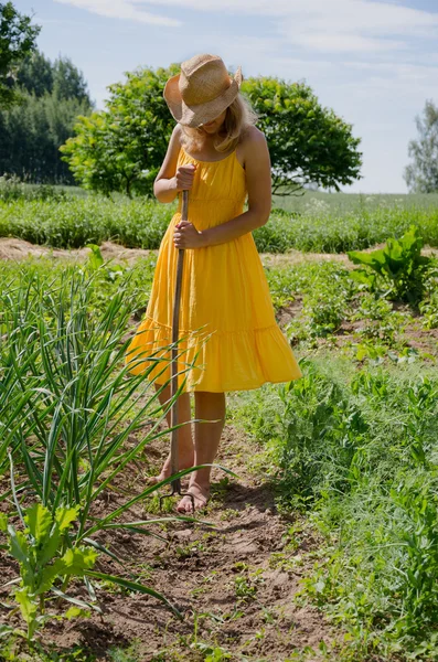 Barefoot vrouw met hoed grub onkruid in de tuin — Stockfoto