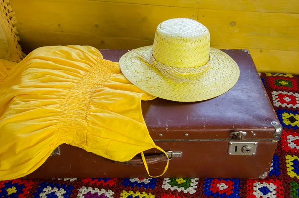 Abito giallo e cappello di paglia sdraiato su vecchia valigia — Foto Stock