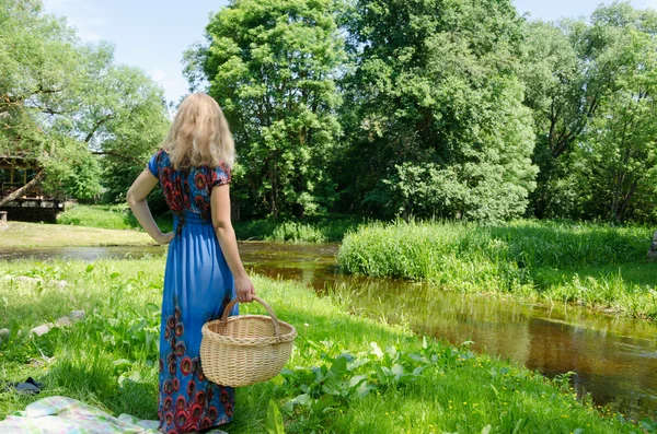 Женщина стоит с плетеной корзиной на лугу — стоковое фото