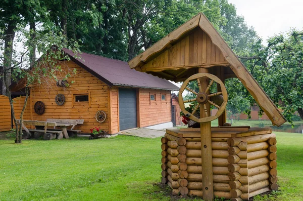 Poço rural decoração de bueiro e casa feita de troncos — Fotografia de Stock