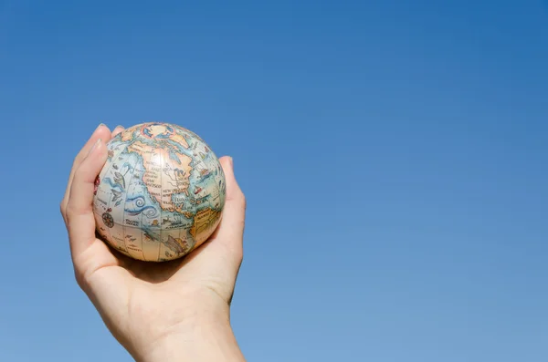 Global earth toy in hand on blue sky background — Stock Photo, Image