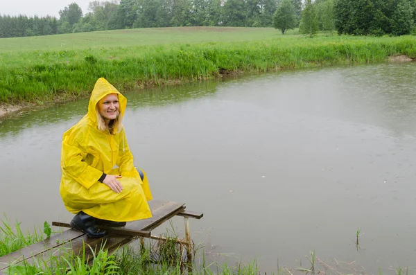 Mädchen auf Fußgängerbrücke zum Teich mit gelbem Regenmantel — Stockfoto