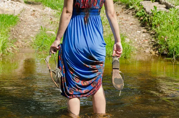 Girl holds sandals wade barefoot flowing stream — Stock Photo, Image