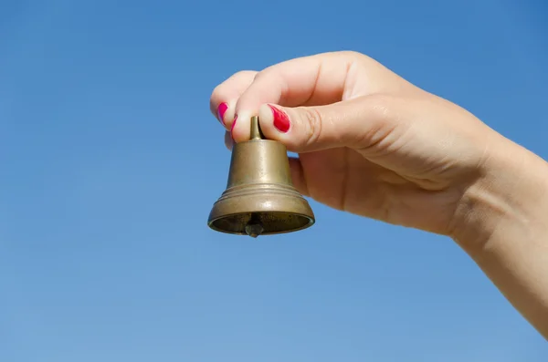 Vrouw hand rode nagels houden ijzer bell op blauwe hemel — Stockfoto