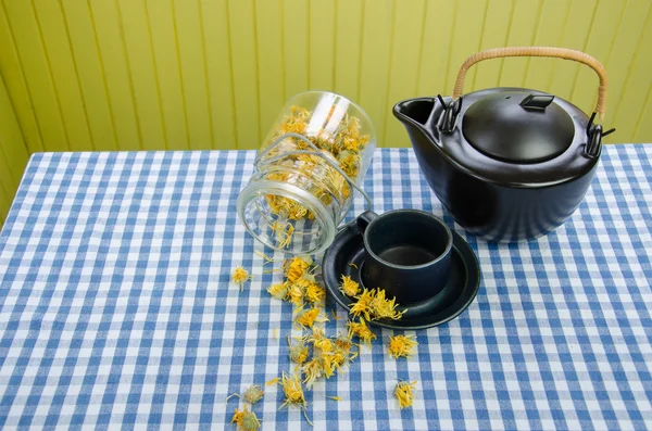 Jar dried coltsfoot on table black ceramic tea pot — Stock Photo, Image