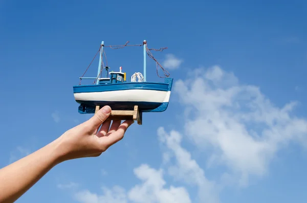 Female hand hold wooden ship toy on sky background — Stock Photo, Image