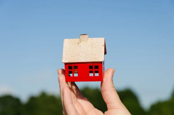 Mano mantenga la casa en miniatura sobre fondo azul cielo —  Fotos de Stock