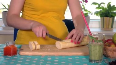 Hamile kadın göbeği ve elleri kesme tahtasındaki bıçakla ekmeği kesiyor.