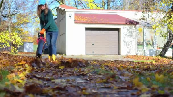 Mujer soplando hojas cerca de su garaje en casa patio trasero — Vídeos de Stock