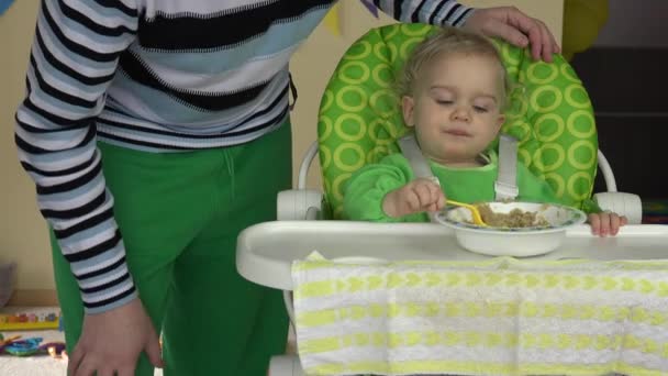 Самотній батько допомагає маленькій дитині їсти кашу пюре з тарілки — стокове відео