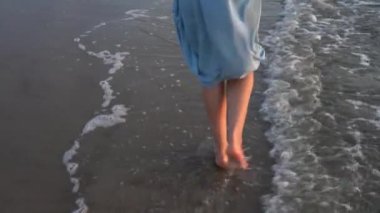 Deniz kıyısında yalın ayak yürüyen ve dalgalarla ıslanan dişi bacakların yakın çekimi.