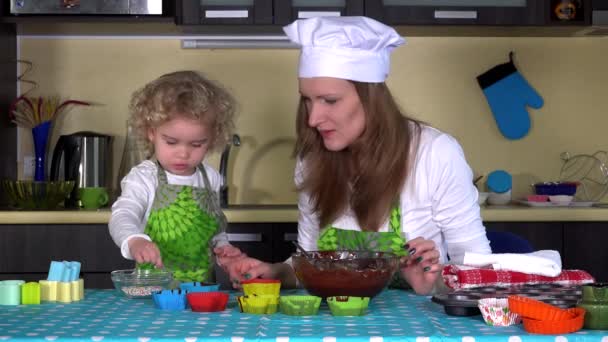 Pó menina polvilha na massa de farinha em moldes de cupcake. mãe ajudante na cozinha. 4K — Vídeo de Stock