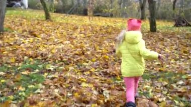 Camera follow little child girl running on autumn covered leaves ground