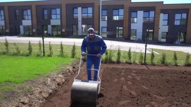Man is using roller to harden ground soil for lawn sowing. Gimbal movement — Stockvideo