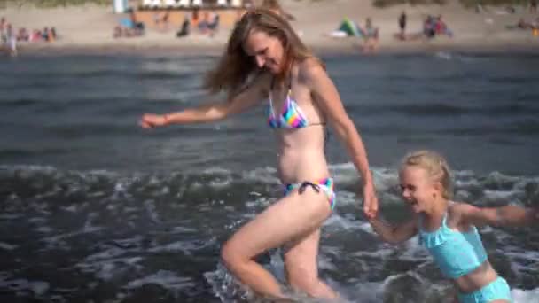 Riendo madre en bikini y niña corriendo a través de las olas — Vídeo de stock