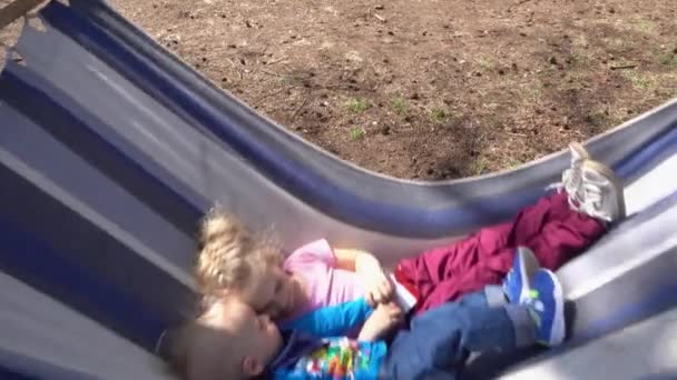 Pár šťastných dětí chlapec a dívka na houpací síti. Sestra a její mladší bratr odpočívají na houpačce. Pohybový výstřel Gimbalového stabilizátoru.