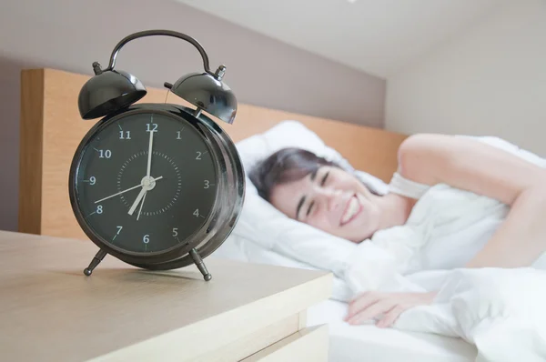 Junge Frau mit Wecker auf dem Bett am Morgen — Stockfoto