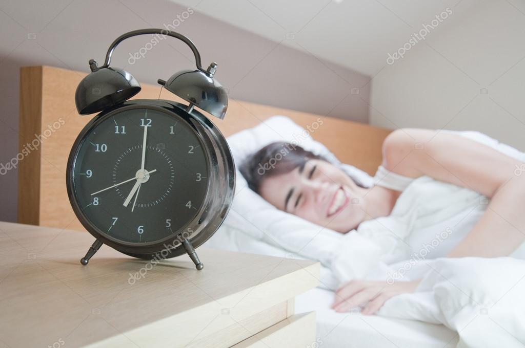 Young woman with alarmclock on the bed at the morning