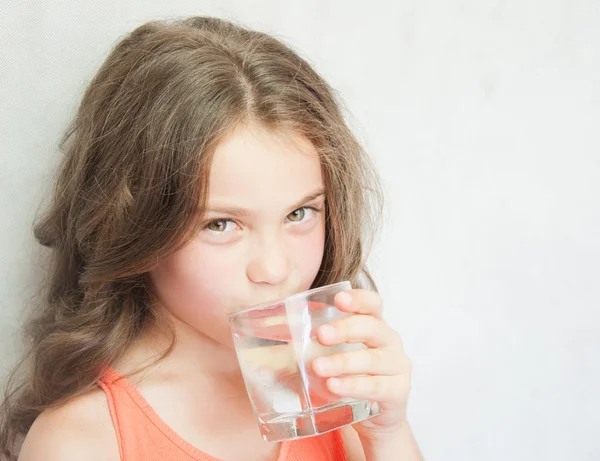 Linda niña bebiendo agua en el fondo gris — Foto de Stock