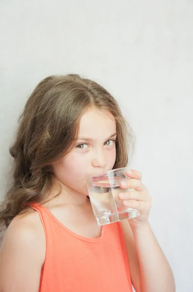 Linda niña bebiendo agua en el fondo gris — Foto de Stock