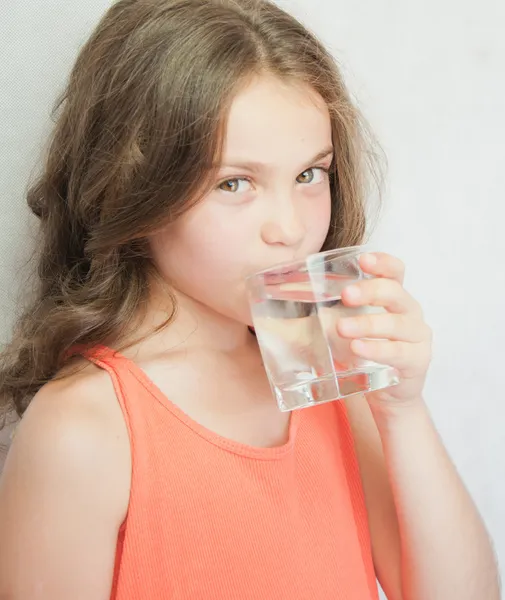 Linda niña bebiendo agua en el fondo gris — Foto de Stock