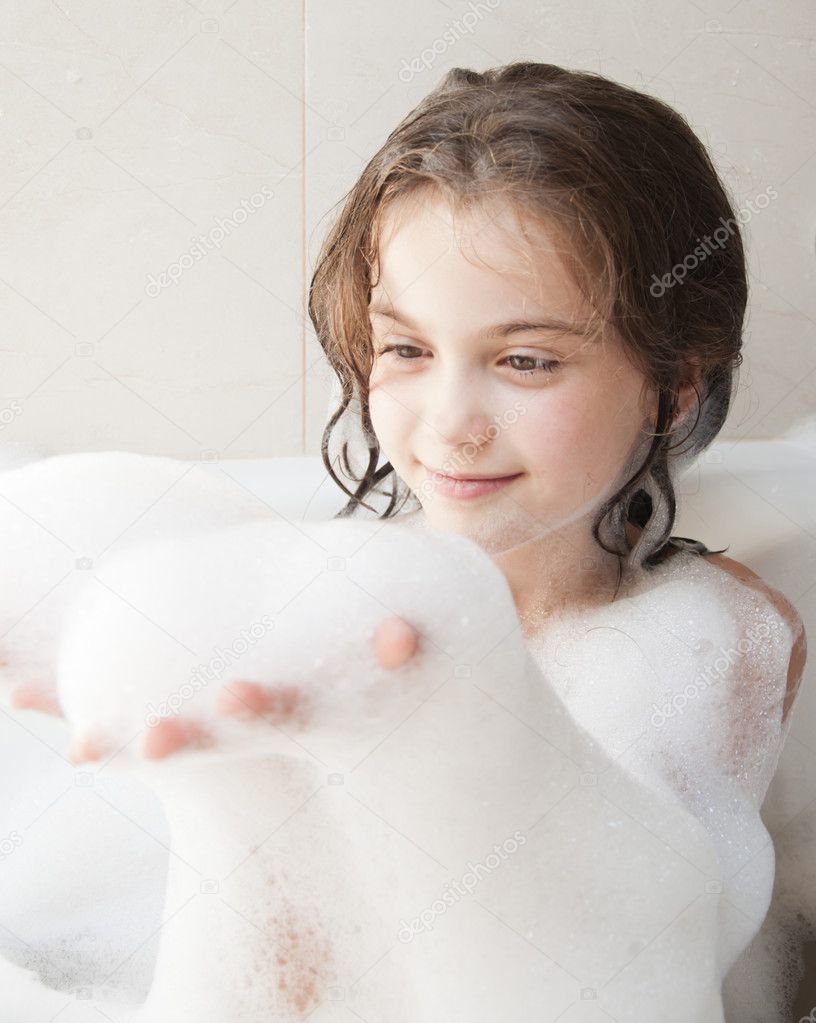 Small pretty girl is taking a bath with a foam